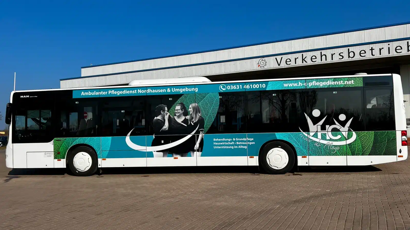 Seitenansicht eines Busses mit Werbung für die ,,Ambulanter Pflegedienst Hund GbR", vor einem Verkehrsgebäude