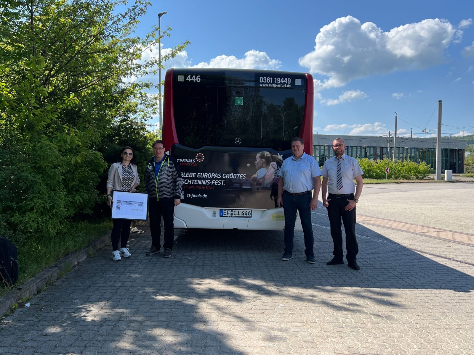 Heckansicht eines Busses mit Werbung für die ,,Tischtennis Marketing GmbH", vier Personen stehen hinter dem Bus