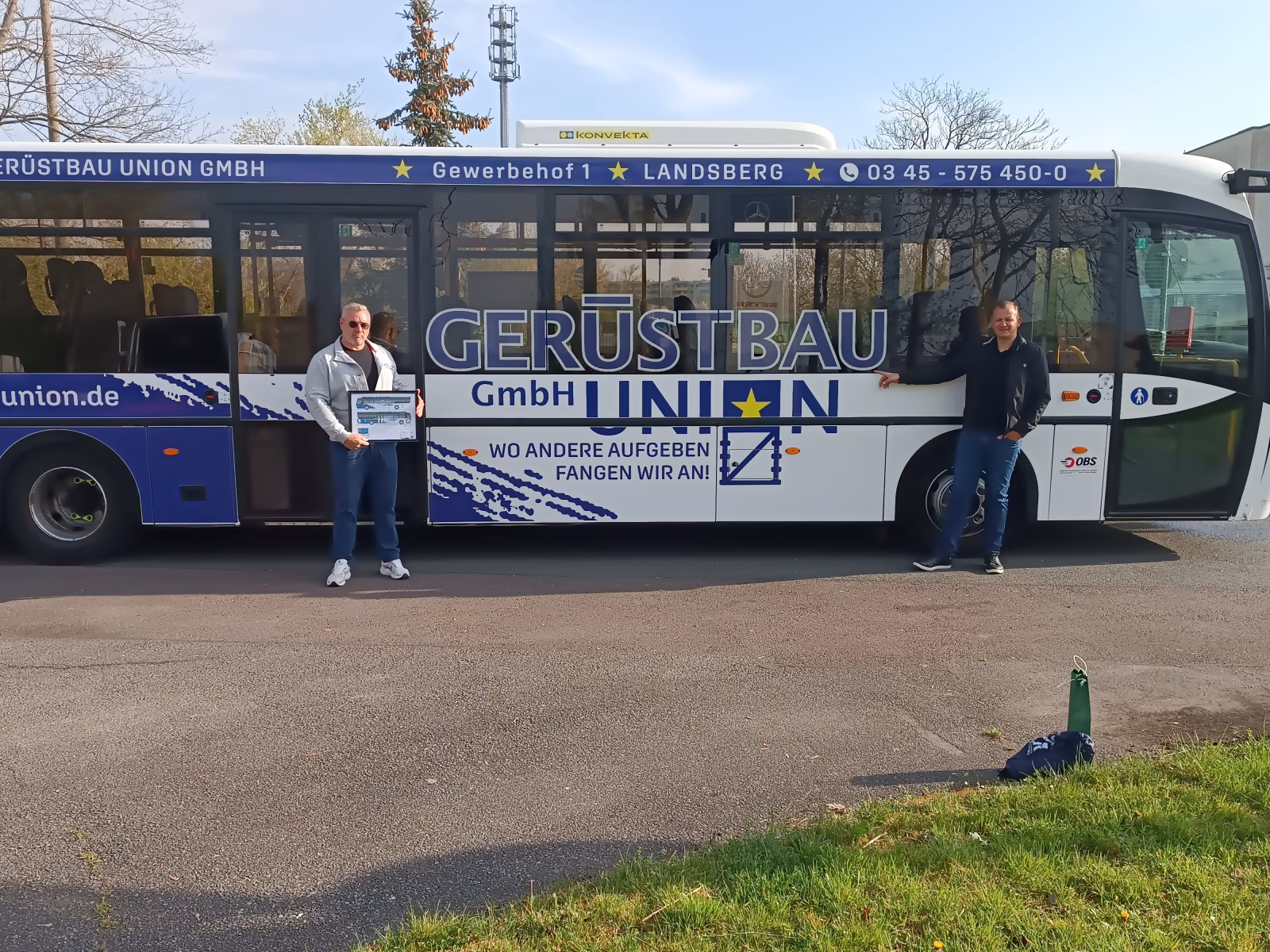Zwei Männer stehen vor einem blauen Bus der Werbung für einen Gerüstbauer macht 