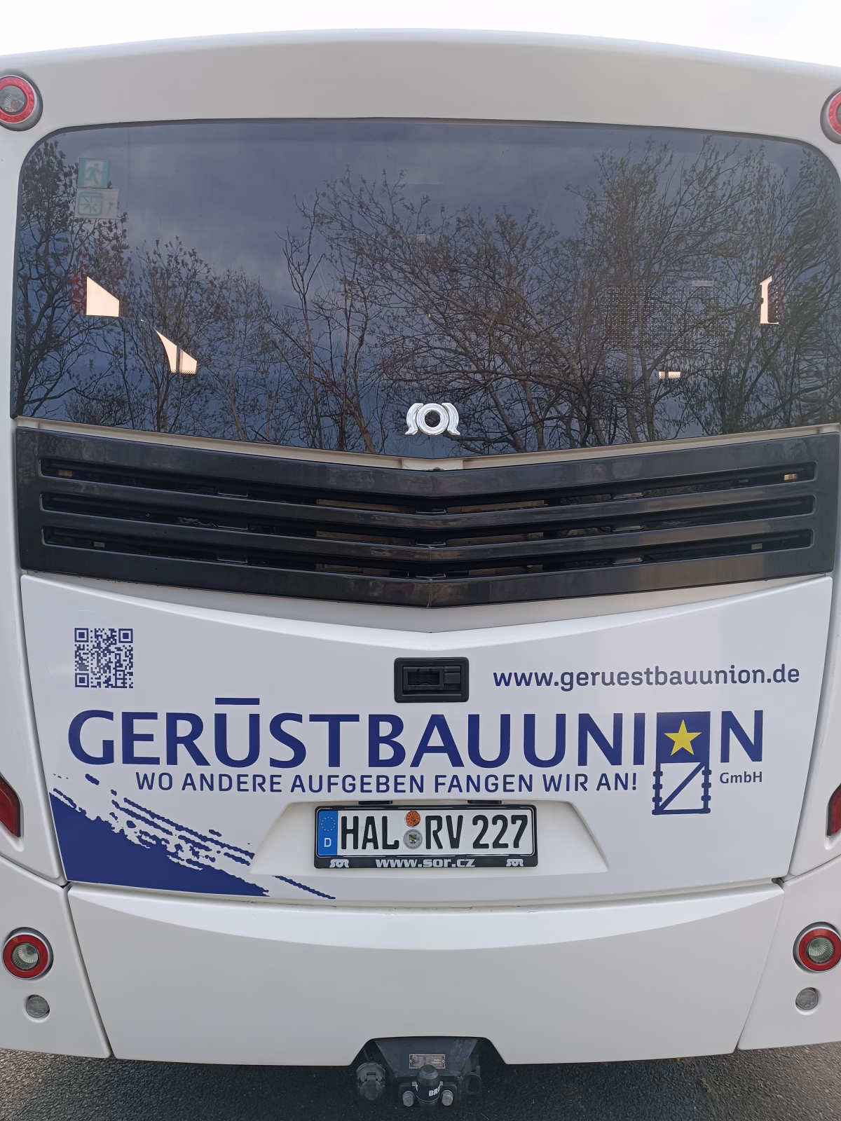 Heckansicht eines blau-weißen Busses der Werbung für einen Gerüstbauer macht 