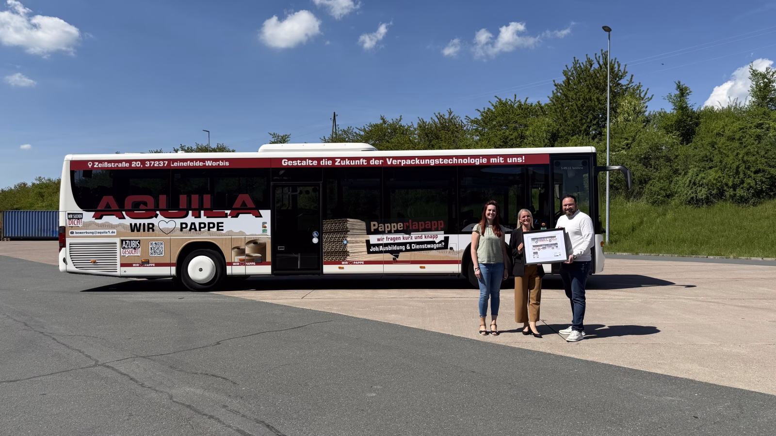 Drei Personen stehen vor einem Bus der Firma Aquila und halten ein Bild dessen in den Händen