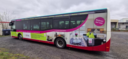 Seitenansicht eines Busses, stehend auf einem Parkplatz mit Werbung für die city4living GmbH