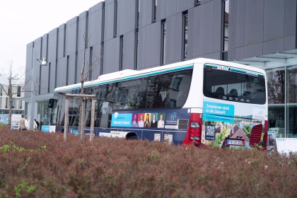 Heckansicht eines Busses mit Werbung für die TH Aschaffenburg, eine Hecke im Vordergrund