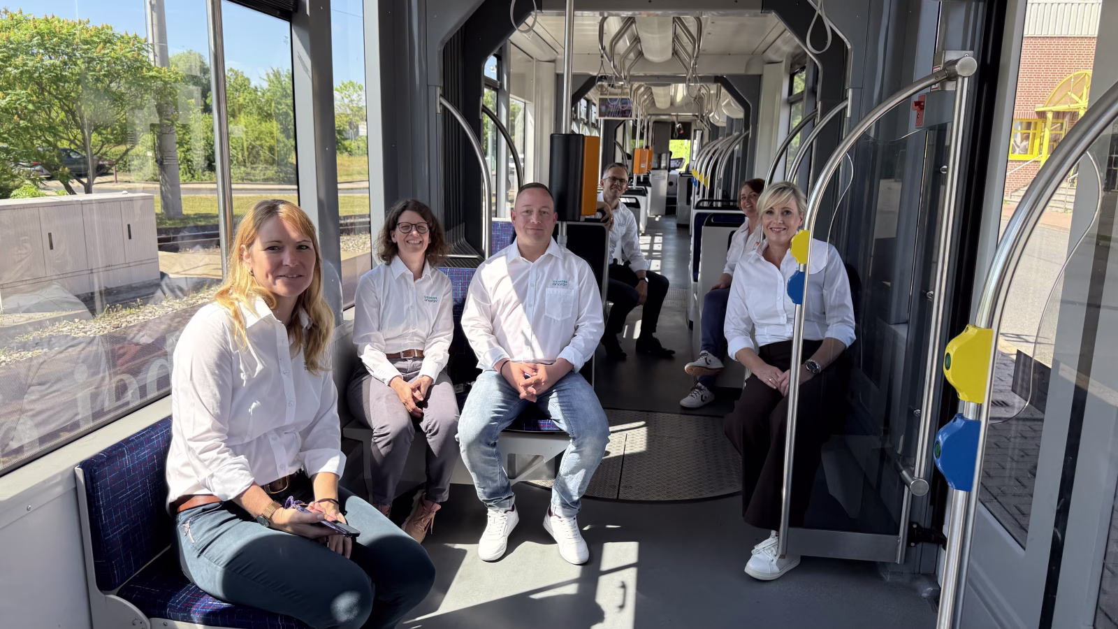 6 Personen mit weißen Hemden sitzen in einer Straßenbahn 