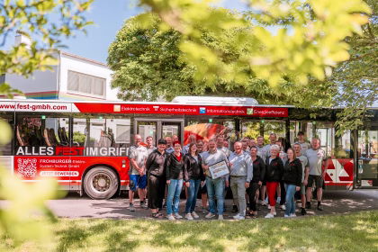 Eine Gruppe von Menschen stehen vor einem roten Bus der Firma FEST