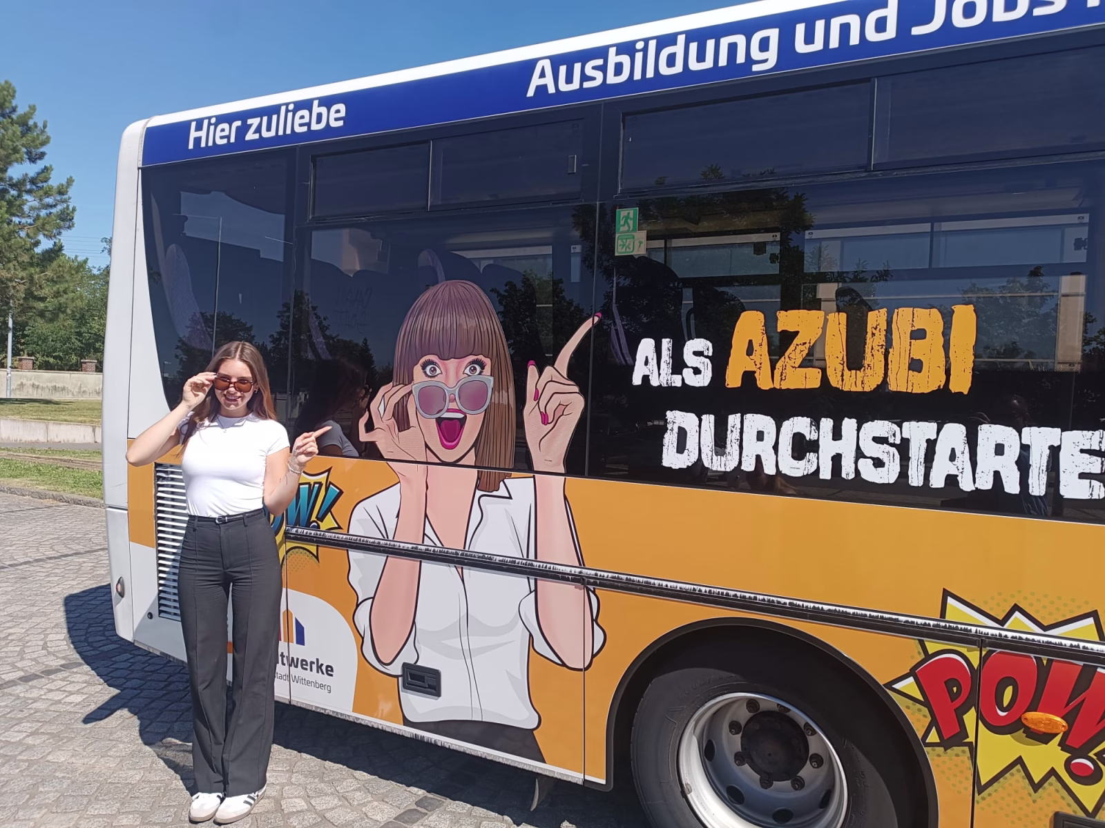 Frau steht vor einem Bus und ahmt eine Karikatur darauf nach 