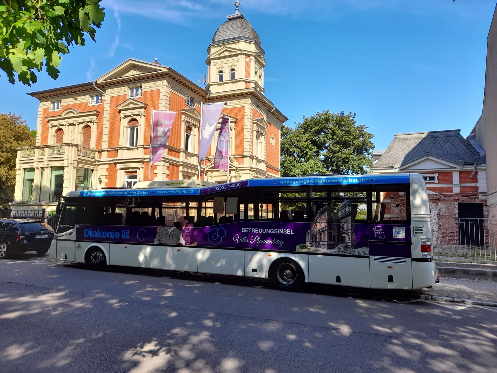 Außenseite eines Busses der Diakonie vor einem historischen Gebäude