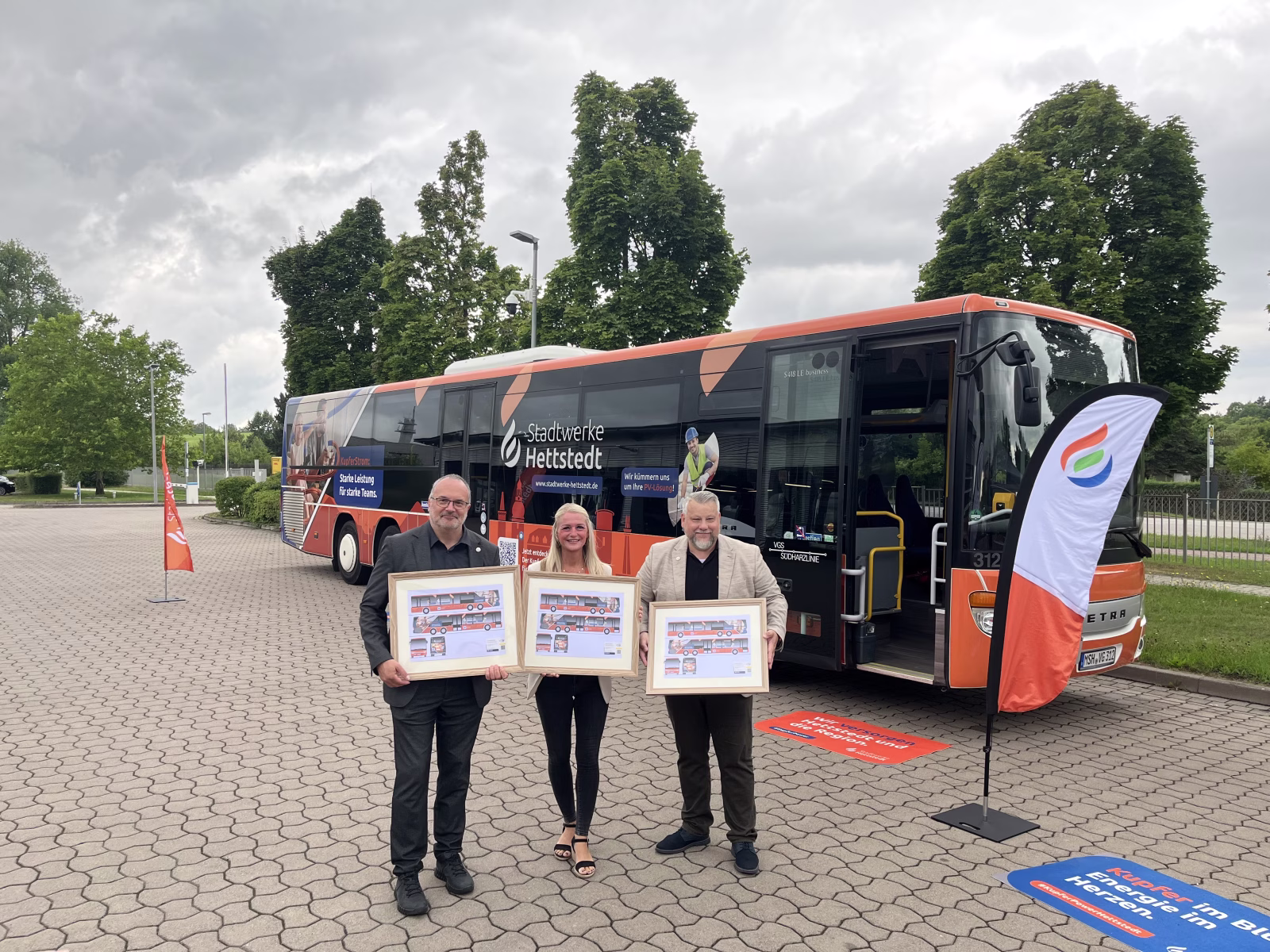 Drei Personen stehen vor einem Bus und präsentieren entsprechende Skizzen des Designs 