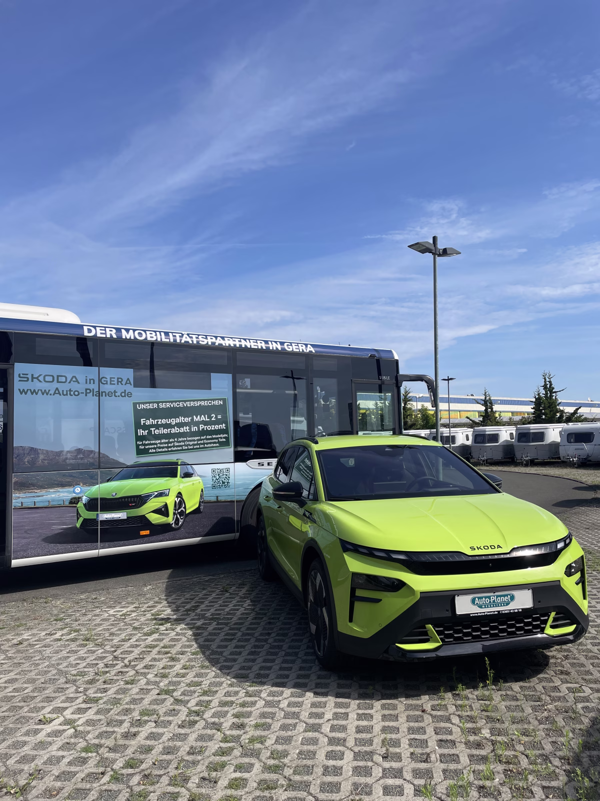 Außenansicht eines Werbebusses vor dem ein grünes Auto steht 