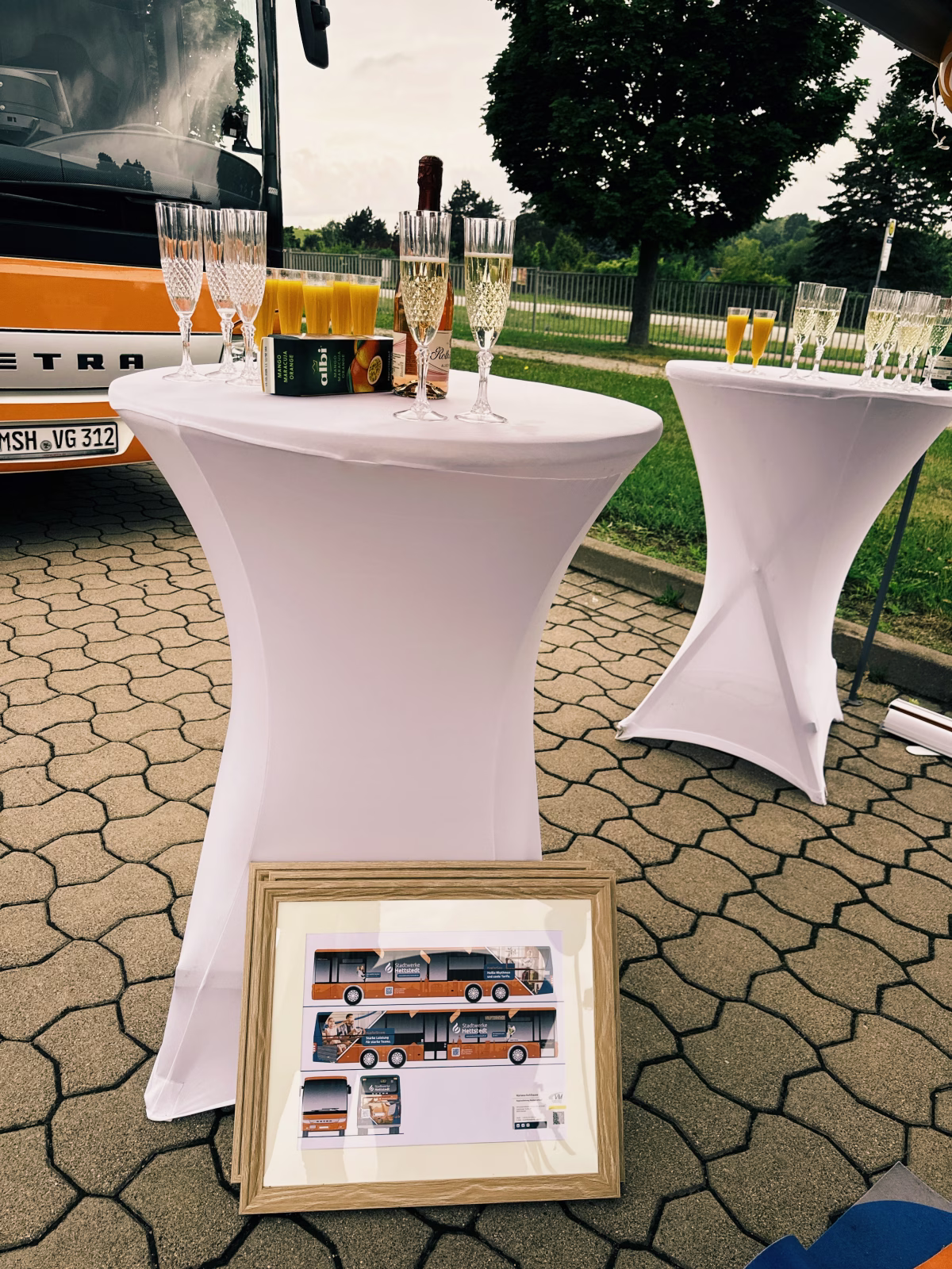 zwei Stehtische mit Sekt stehen vor einem Bus 