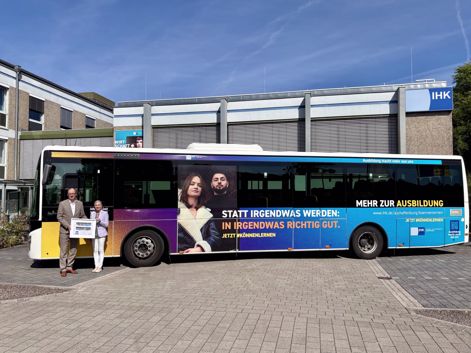 Zwei Personen stehen vor einem Bus und präsentieren ein Plakat dessen