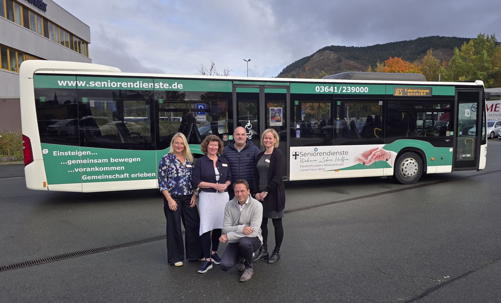 5 Personen stehen mit einer eingerahmten Grafik eines Werbebusses vor diesem Bus