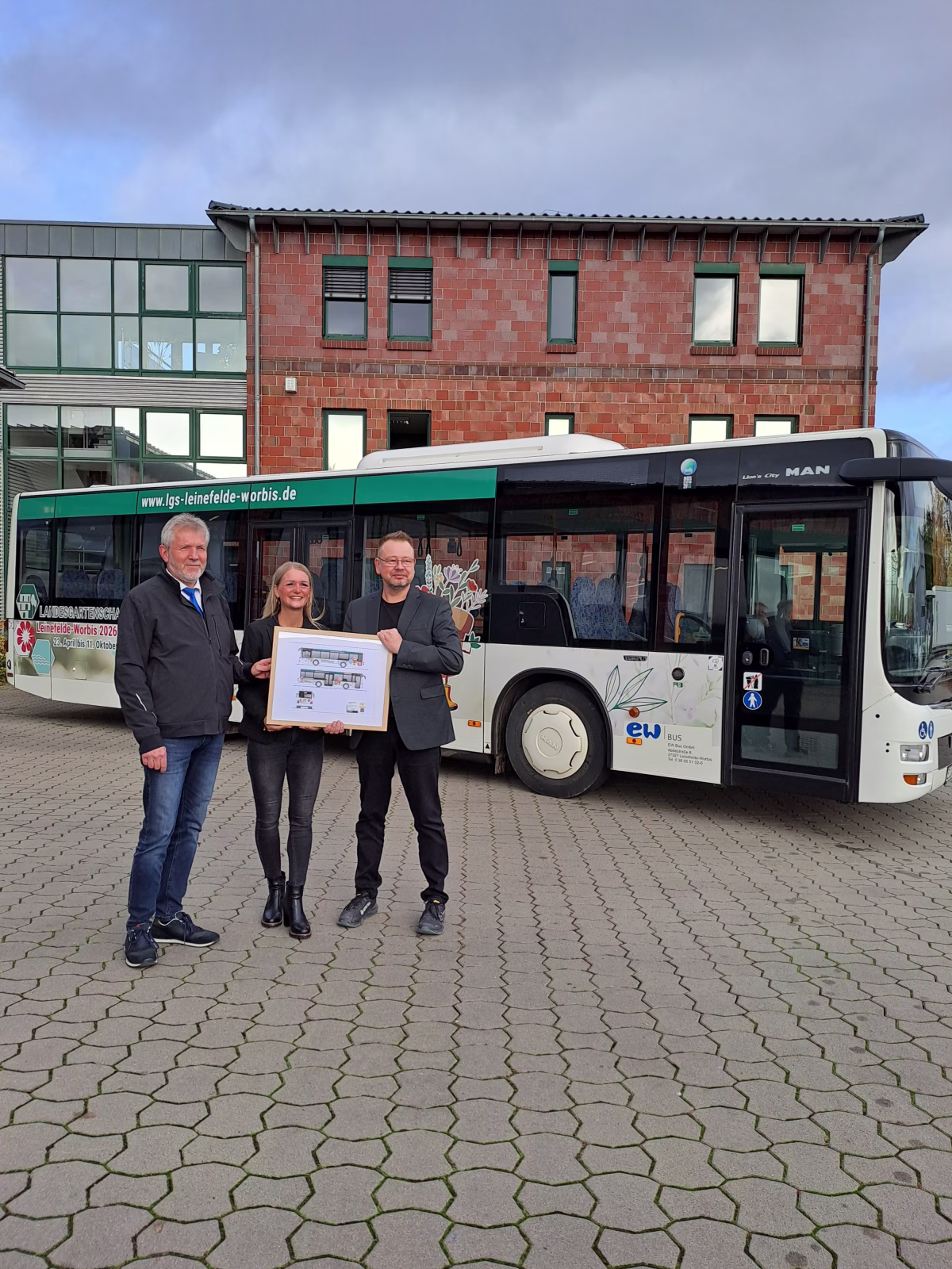 Drei Personen stehen vor einem Werbebus und halten ein Bild dessen hoch