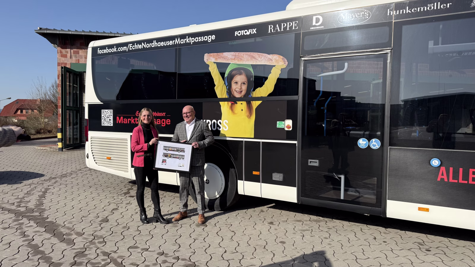 Zwei Personen stehen mit einer Grafik des Busses vor dem Bus der Nordhäuser Marktpassage