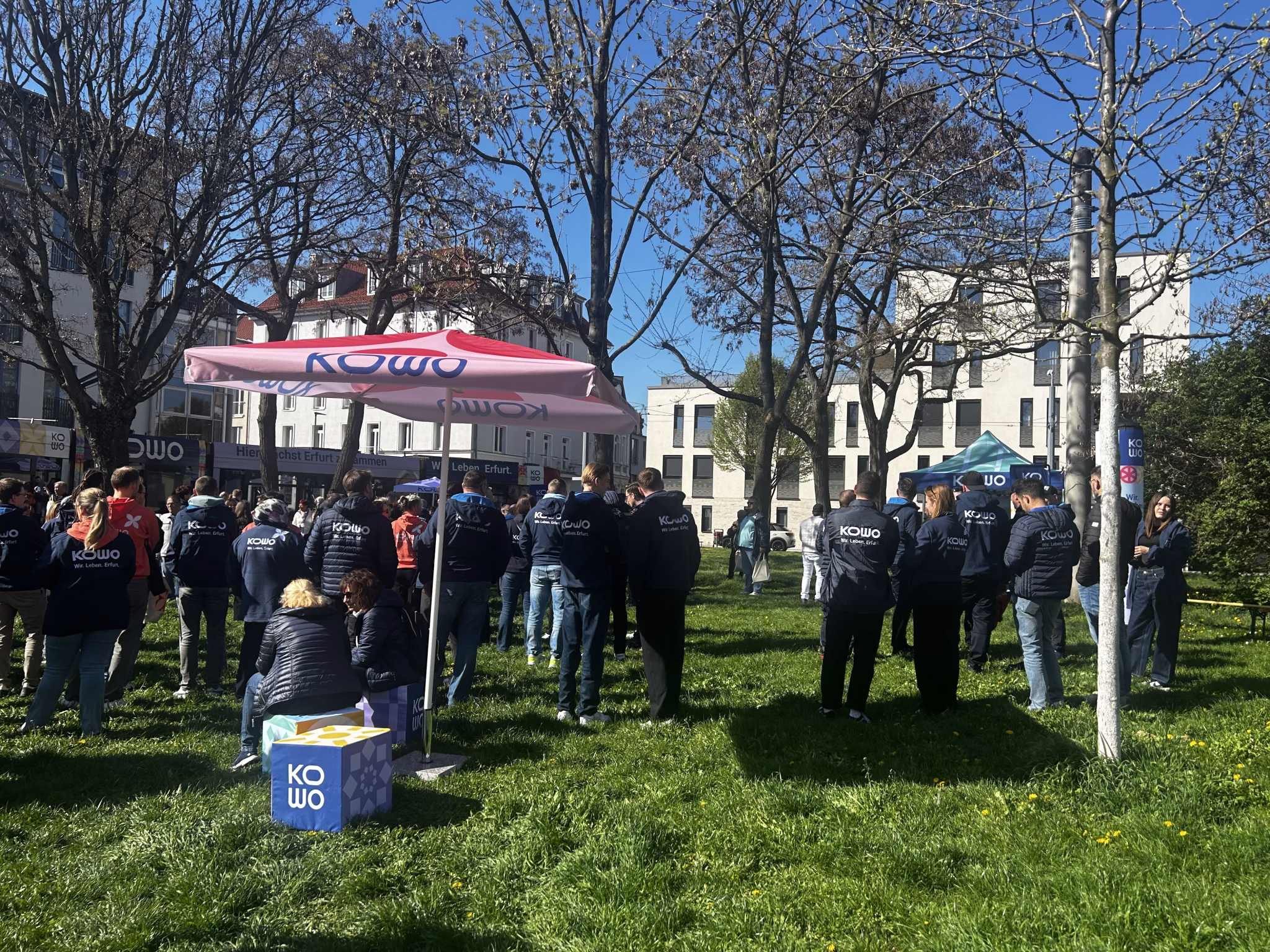 Eine große Gruppe von Personen steht auf einer Wiese mit einem Pavillion der KOWO Erfurt