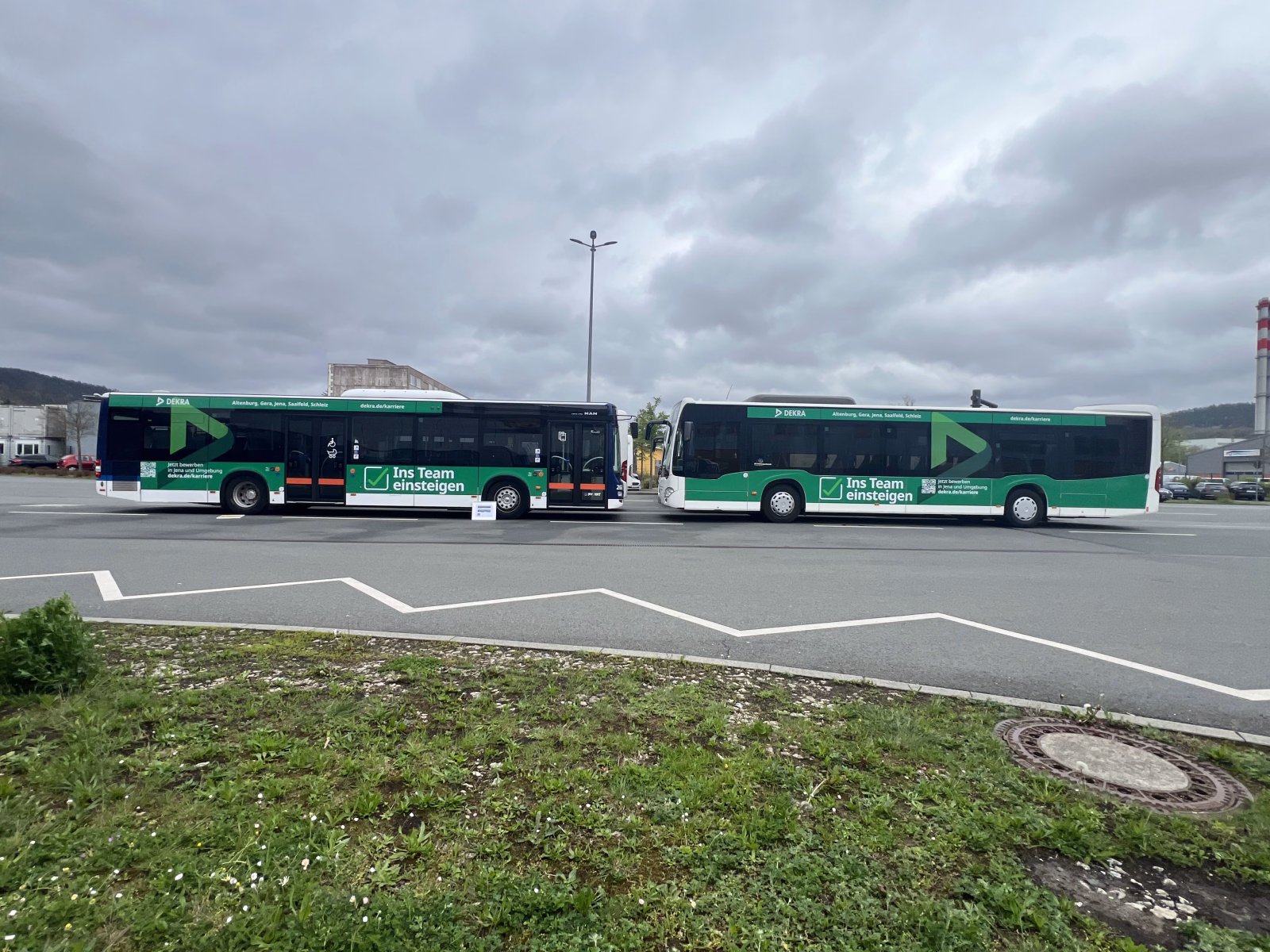 zwei grüne Busse der DEKRA Jena stehen auf einem Parkplatz