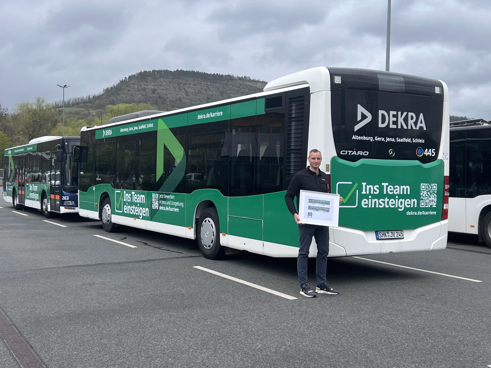 Ein Mann steht vor einem grünen Bus mit Werbung der DEKRA Jena