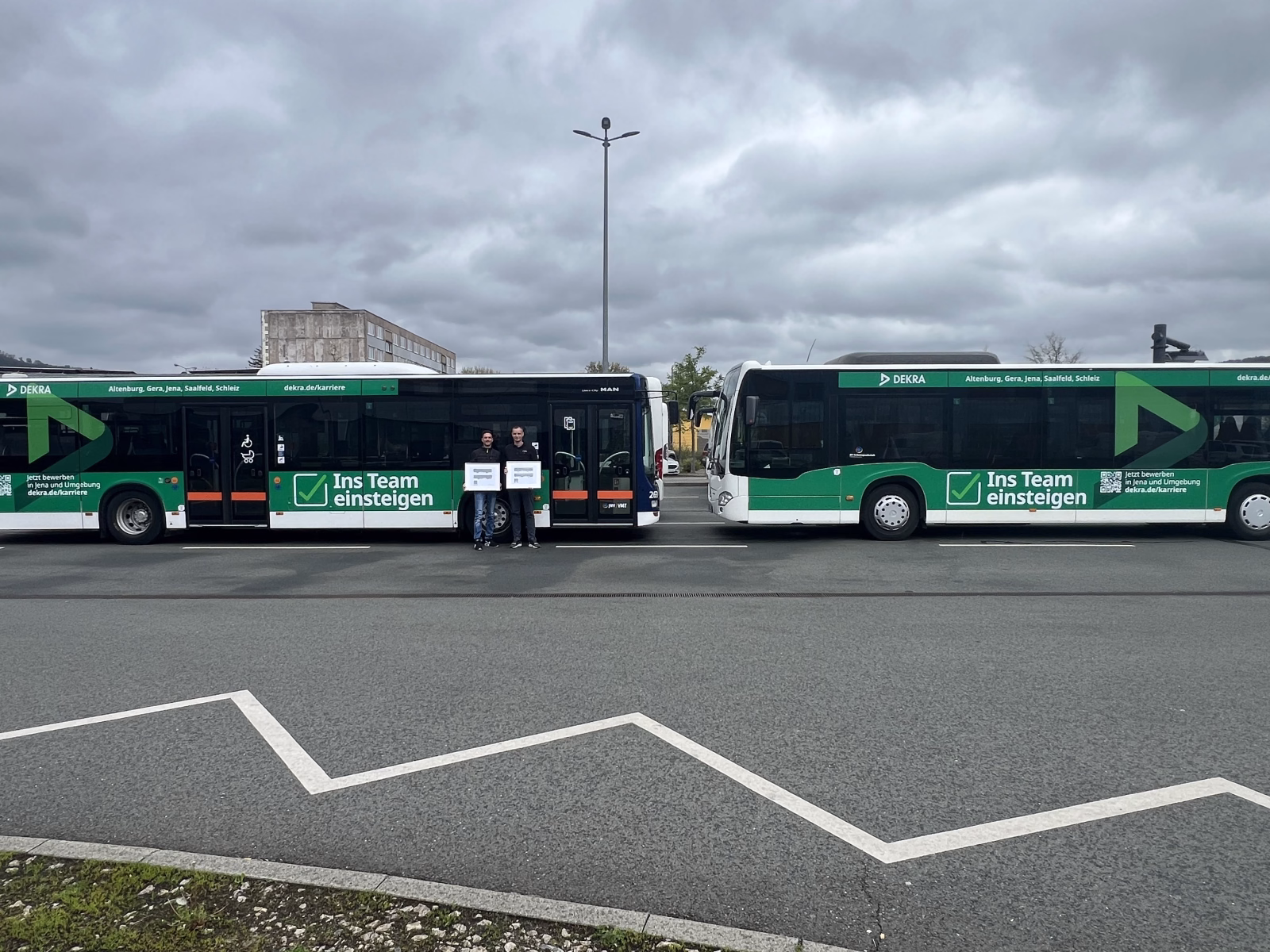 Zwei Männer stehen vor zwei grünen Bussen der Dekra Jena auf einem Parkplatz