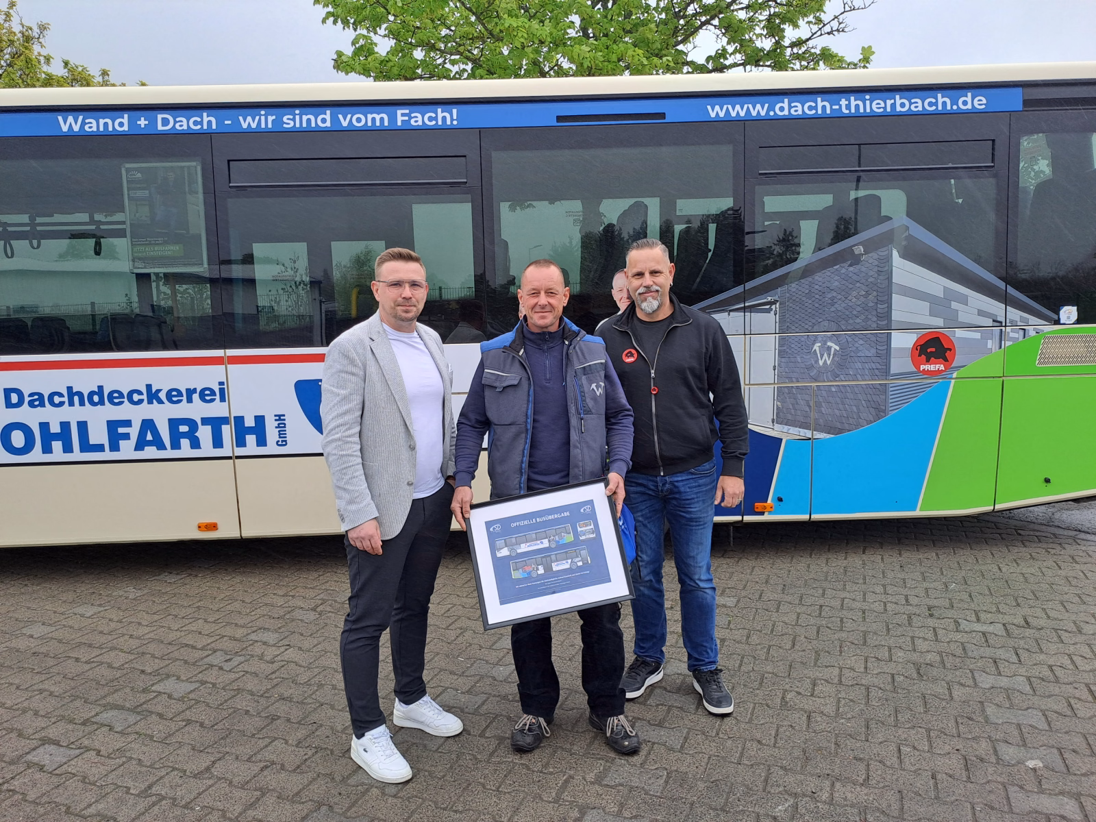 Drei Personen stehen vor einem Bus mit Werbung der Dachdeckerei Wohlfarth