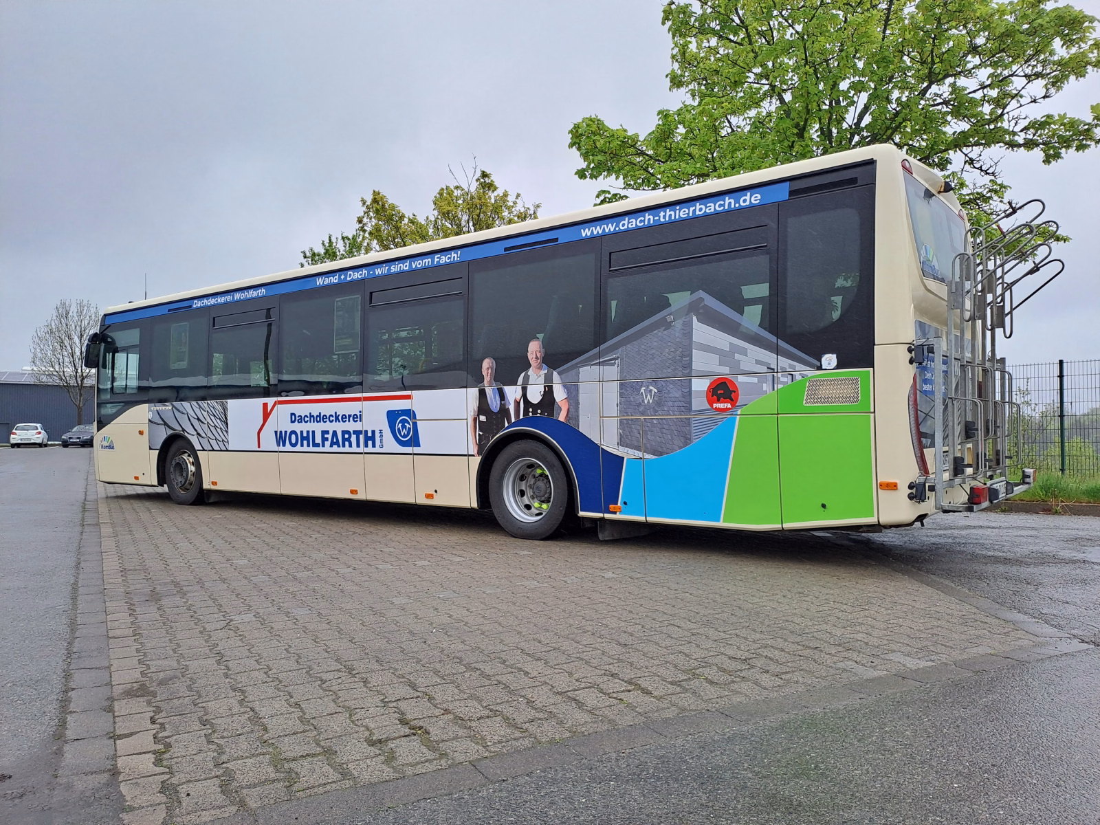 Außenseite eines Beigen Busses mit Werbung der Dachdeckerei Wohlfahrt
