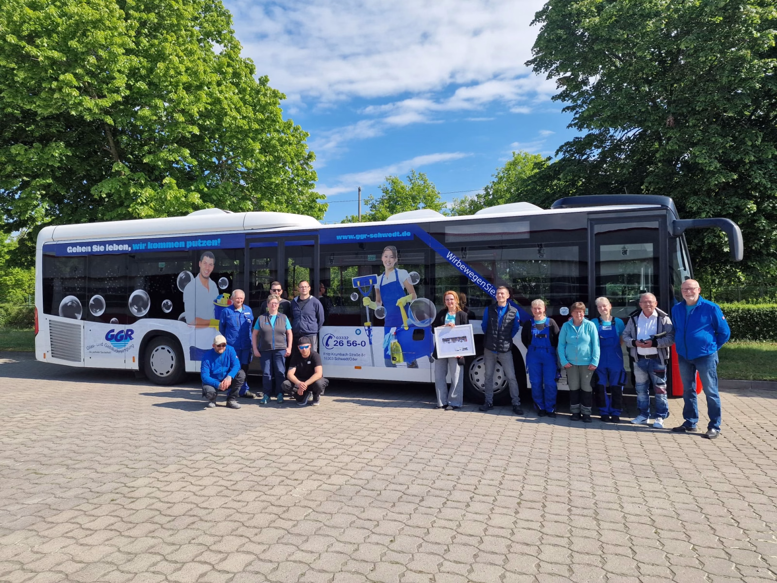 Eine Gruppe von Menschen posiert vor einem Werbebus mit Werbung des Glas- und Gebäudereinigungs GmbH