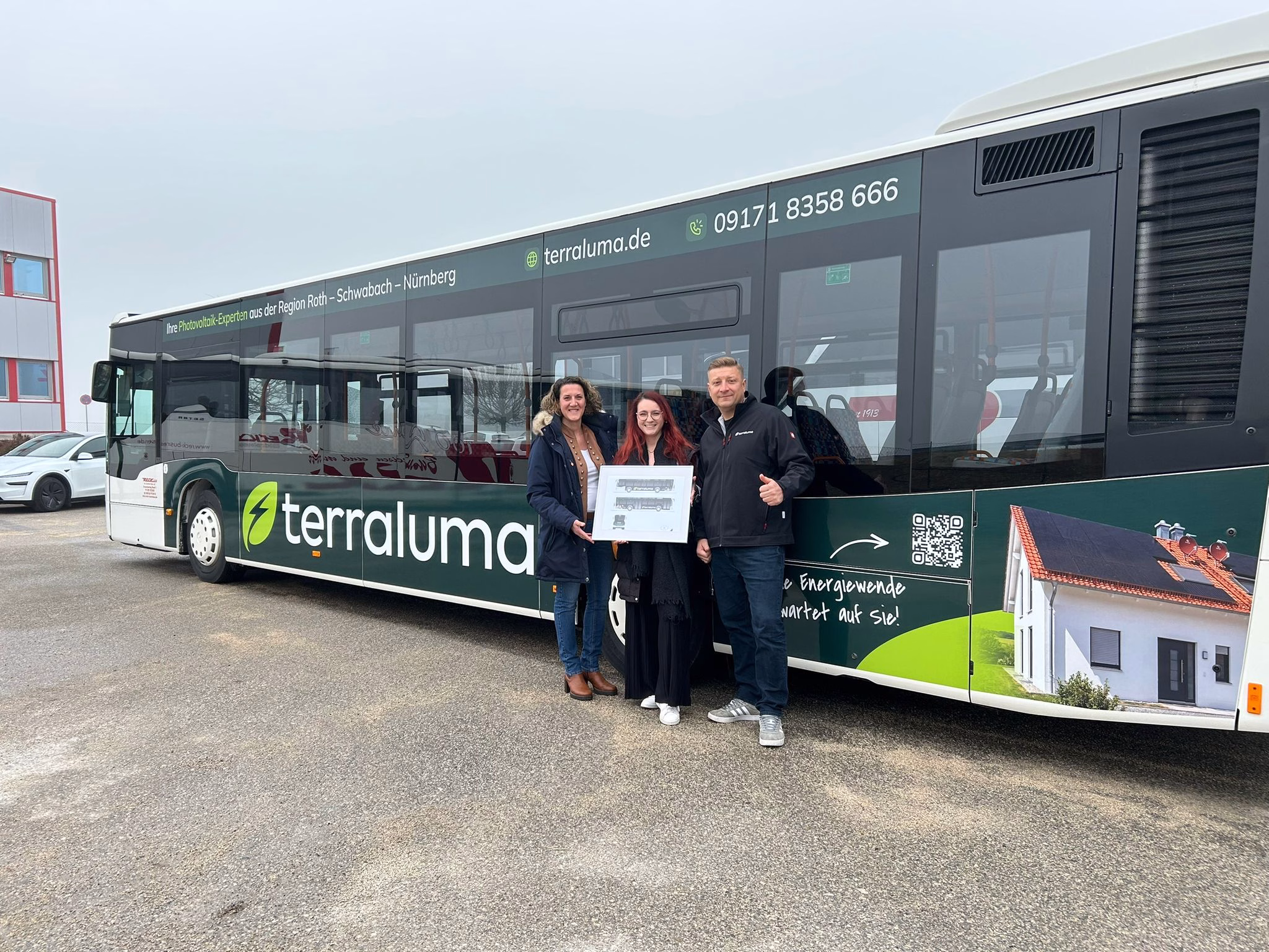 Drei Personen stehen vor der Außenseite eines dunklen Busses mit Werbung der terraluma GmbH