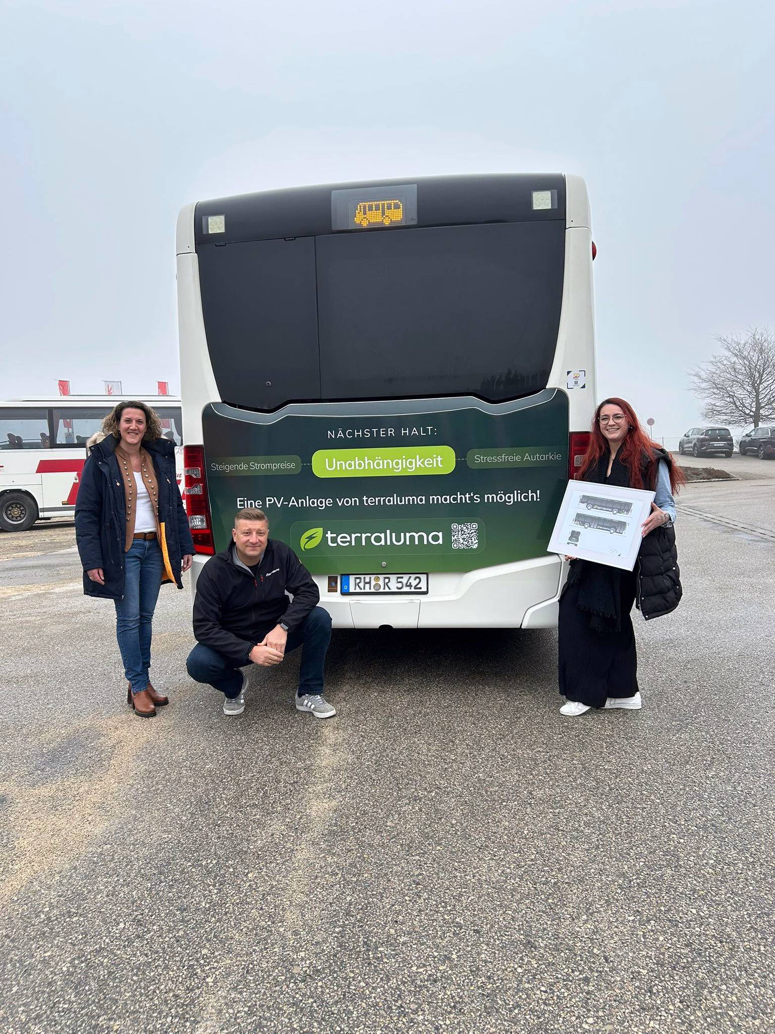 Drei Personen stehen vor dem Heck eines dunklen Busses mit Werbung der terraluma GmbH