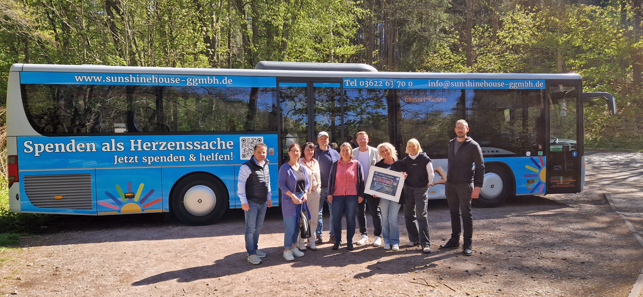 Eine Gruppe von Personen stehen vor einem blauen Bus mit Werbung der sunshinehouse ggmbh