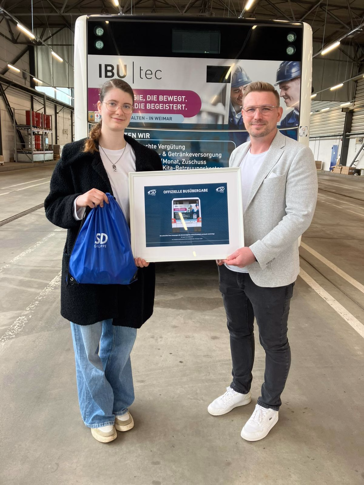Zwei Personen stehen vor einem Busheck mit Werbung der IBU-TEC GmbH