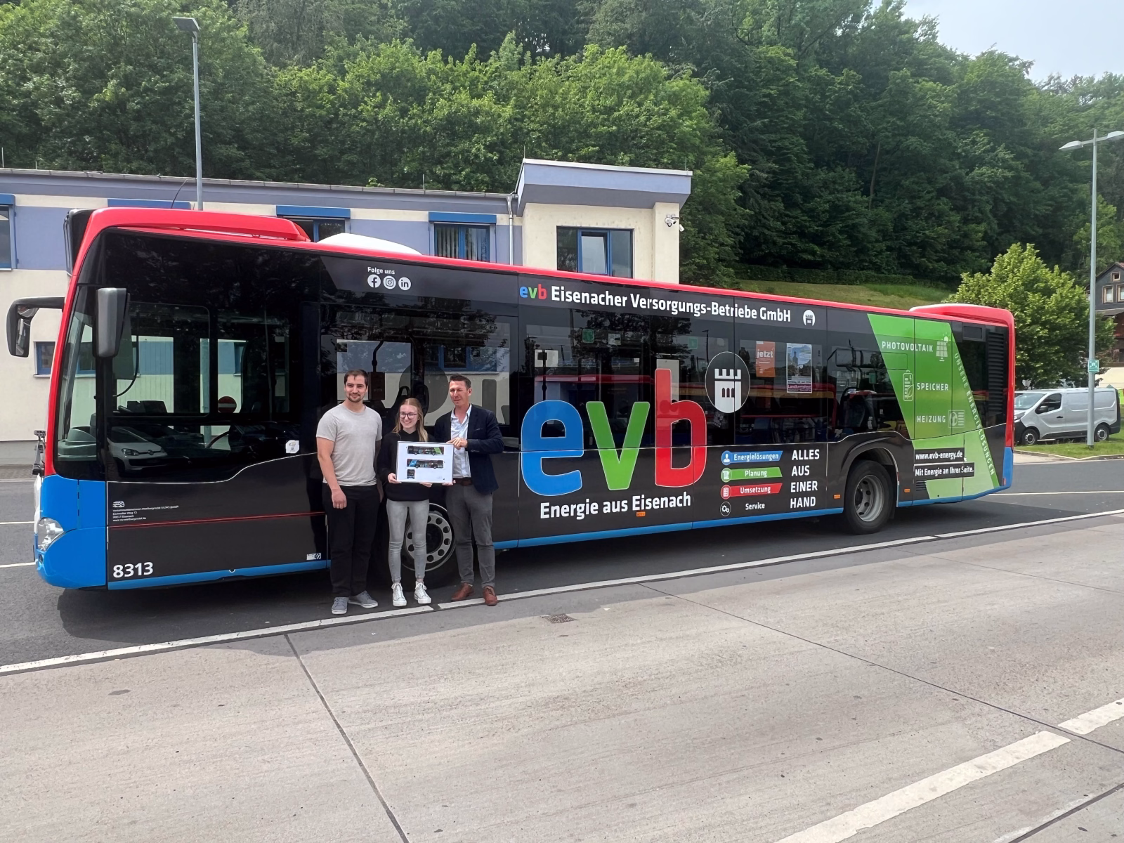 Drei Personen stehen vor einem dunklen Werbebus der evb GmbH