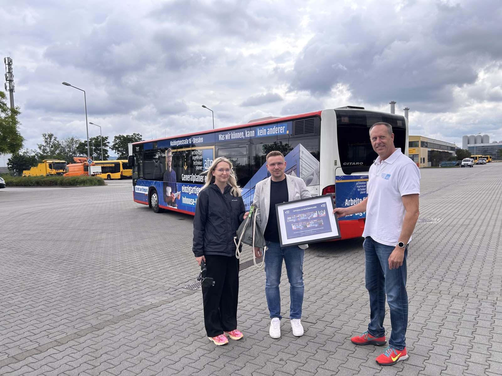 Drei Personen stehen auf einem Parkplatz vor einem Stadtbus mit Werbung der aitp Dresden