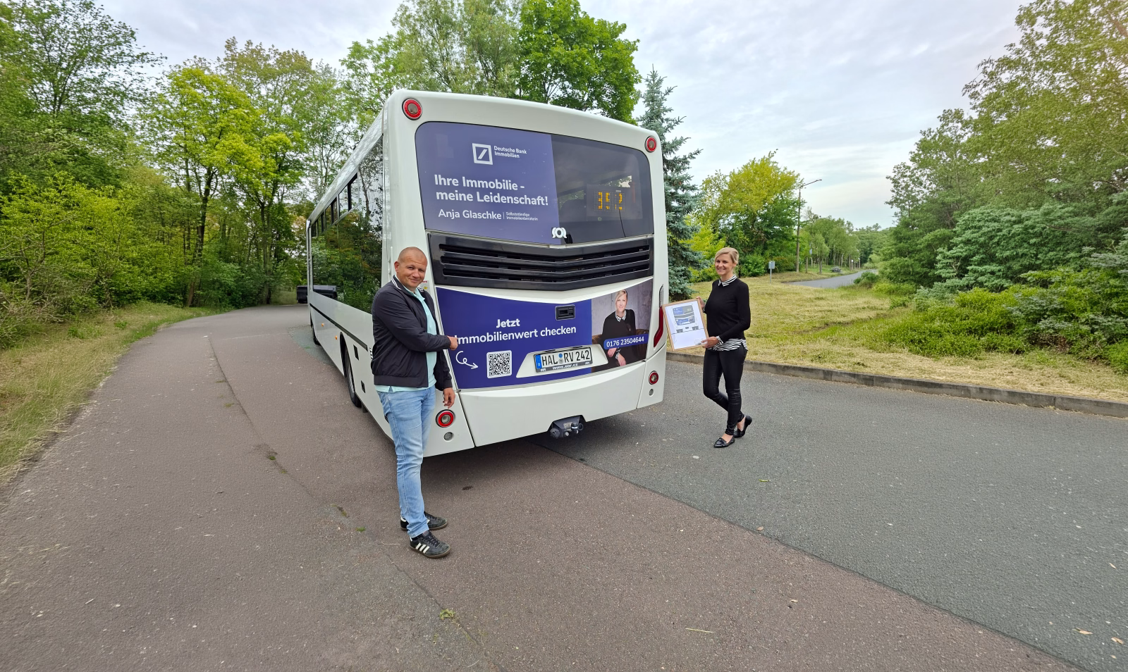 Zwei Personen stehen am Heck eines weißen Werbebusses mit Aufschrift der Deutschen Bank Immobilien