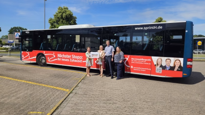 Vier Personen stehen an der Außenseite eines roten Busses mit Werbung der Sparkassen Immobilien Vermittlung Hannover