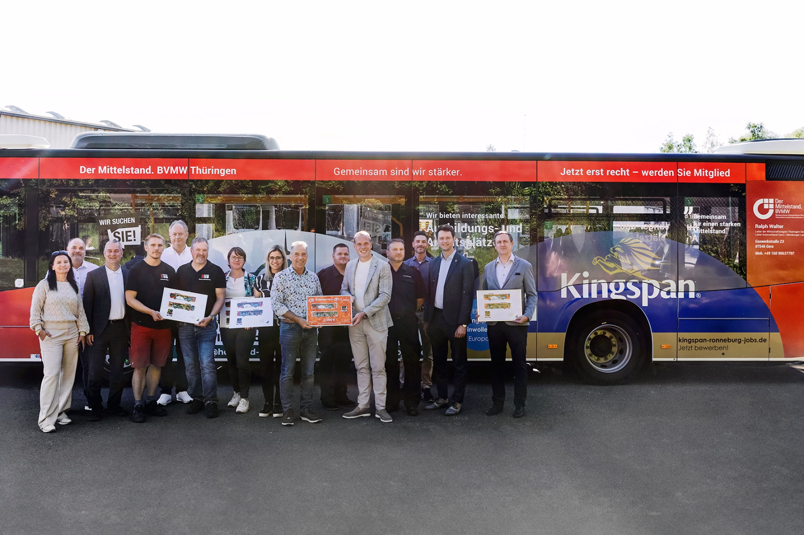 Eine Gruppe von Menschen steht vor einem blau, roten Bus mit Werbung des BVMW