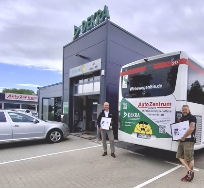 Zwei Personen stehen vor einem Gebäude der DEKRA Templin und posieren vor einem Bus mit dazu passender Werbung