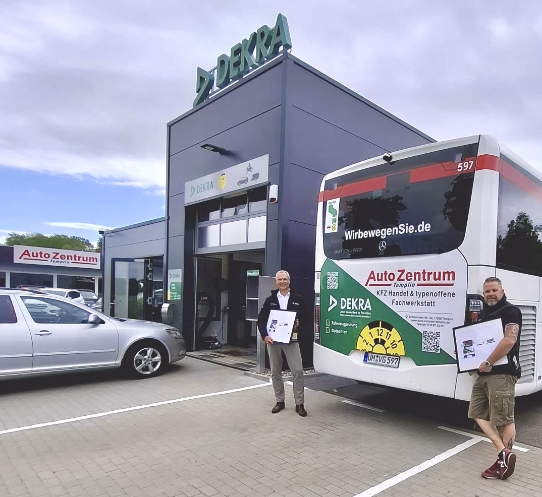 Zwei Personen stehen vor einem Gebäude der DEKRA Templin und posieren vor einem Bus mit dazu passender Werbung