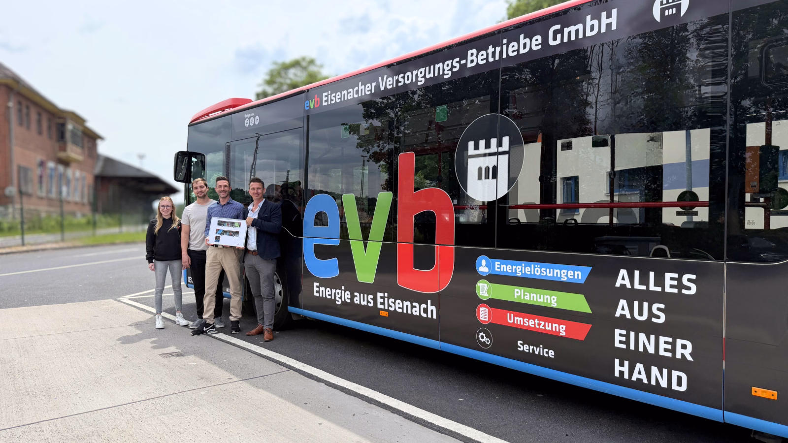 vier Personen stehen auf einem Parkplatz vor einem dunklen Werbebus der evb GmbH
