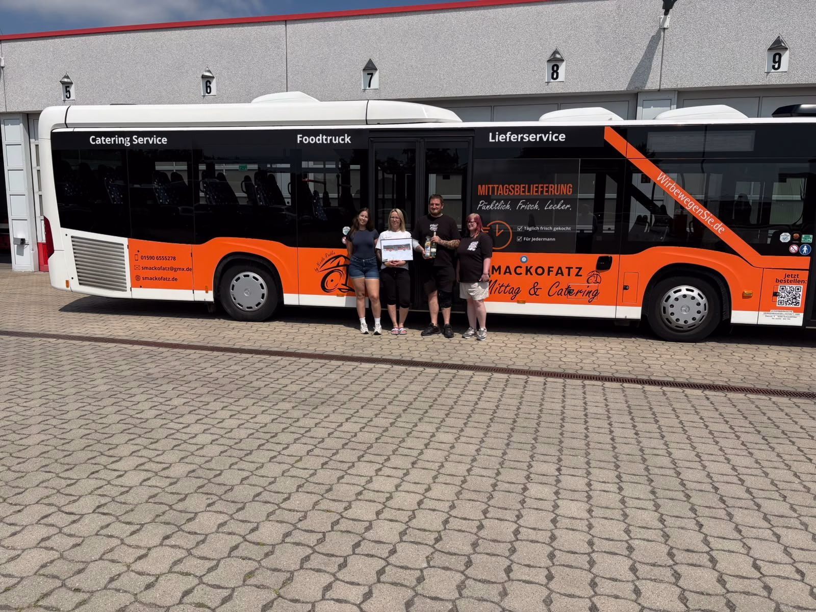 Vier Personen stehen vor der Einstiegsseite eines organenen Stadtbusses
