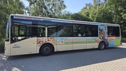 Außenansicht eines beigen Busses mit grüner Werbung von Maler&Parkett Wachter