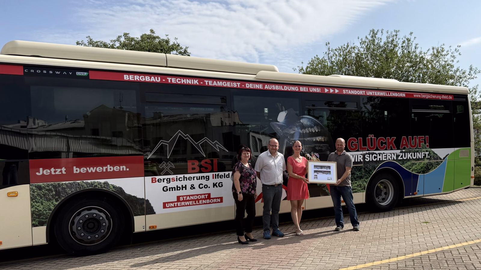Vier Personen stehen vor einem Stadtbus mit Werbung der Bergsicherung Illfeld
