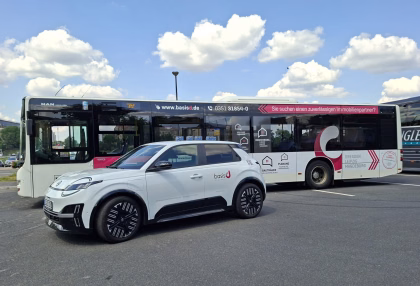 Ein Firmenauto des Immobilienmaklers basis d steht vor einem Stadtbus mit der gleichen Unternehmenswerbung
