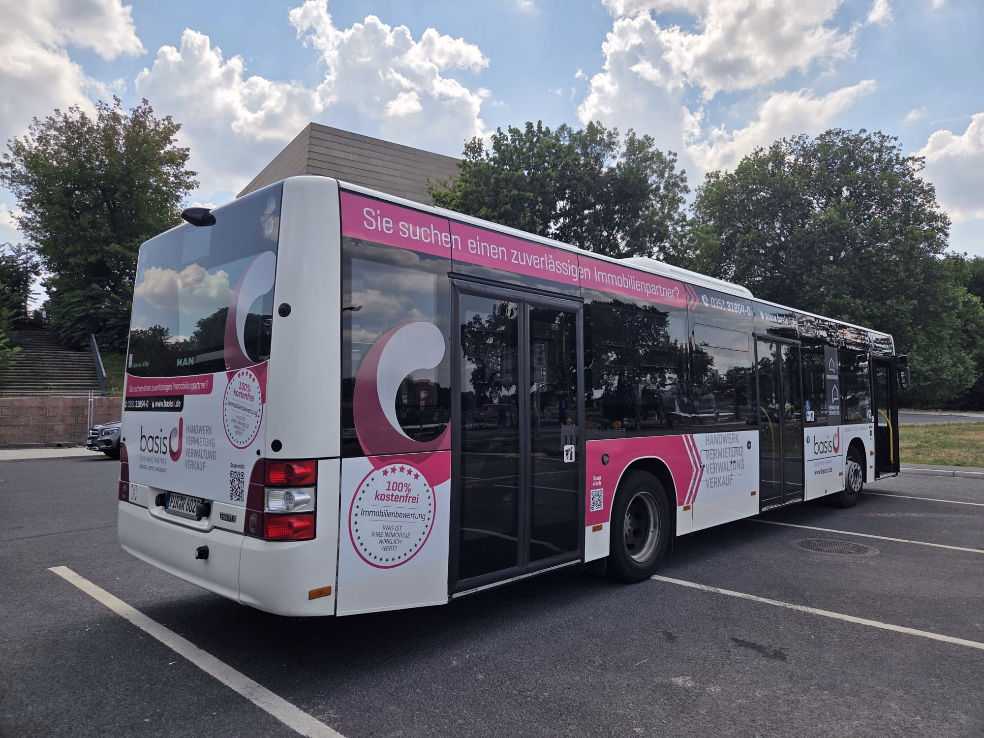 Einstiegsseite und Heck eines rosa/weißen Busses mit Werbung von Basis d