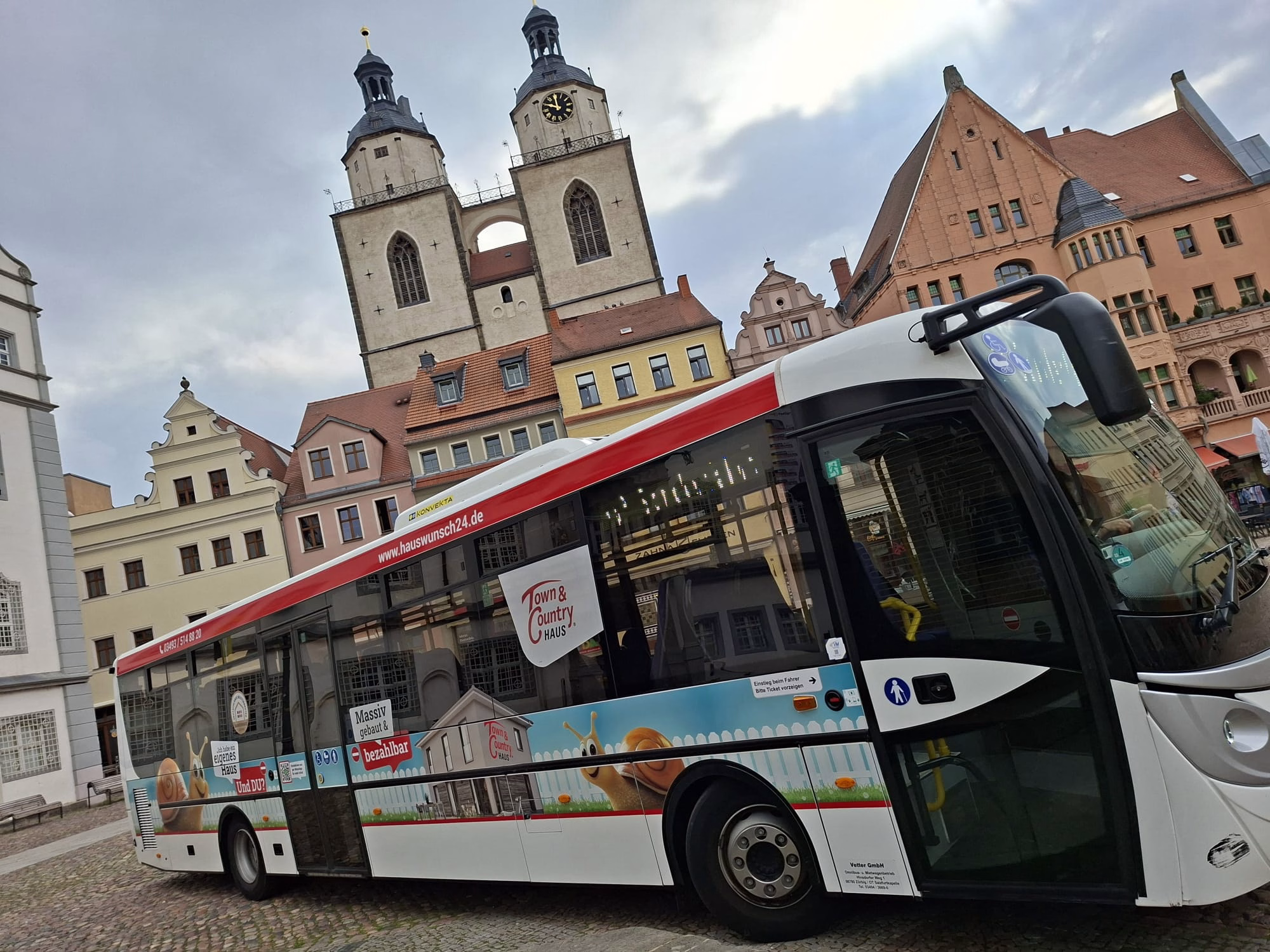 Einstiegsseite eines weißen Busses mit Werbung der HIS Hausbau GmbH