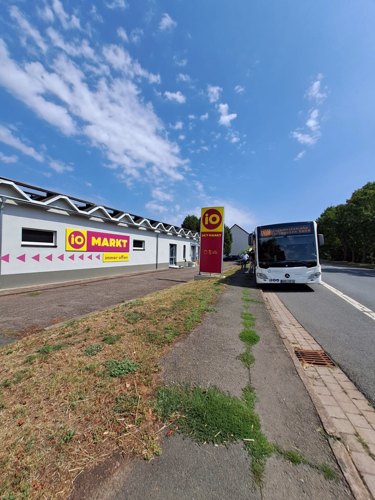 ein weißer Stadtbus steht an einer Haltestelle vor dem io Markt