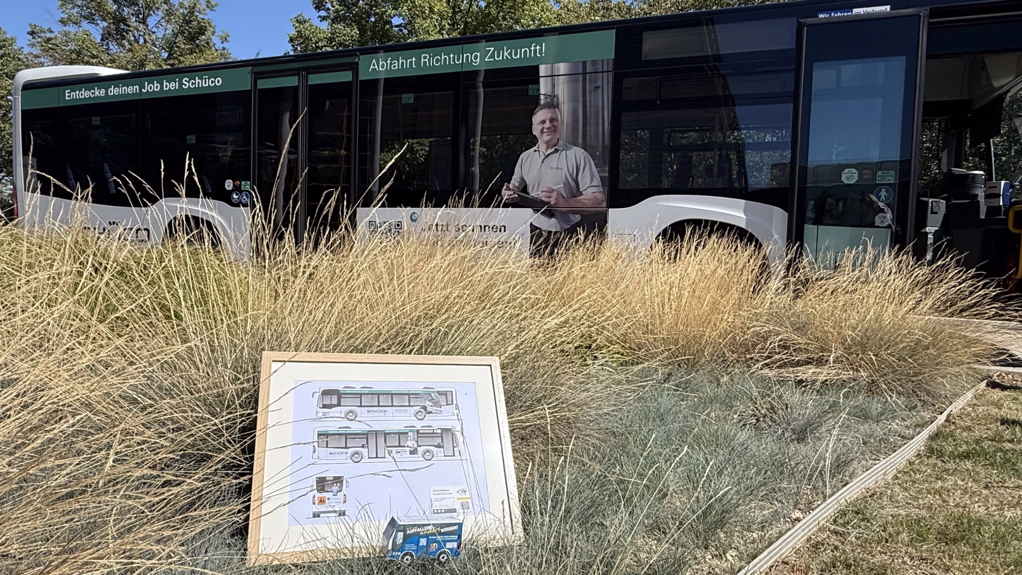 Ein Bus der Schüco Polymer Technologies steht vor einem Blumenbeet mit einer Fotografie des Busses