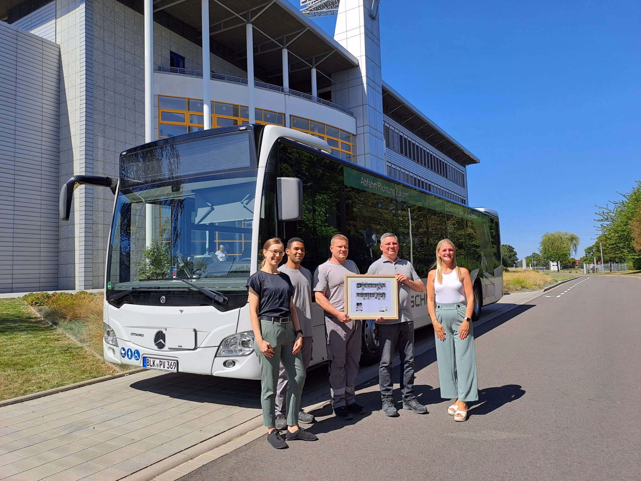 Fünf Personen stehen vor einem weißen Stadtbus und lächeln in die Kamera