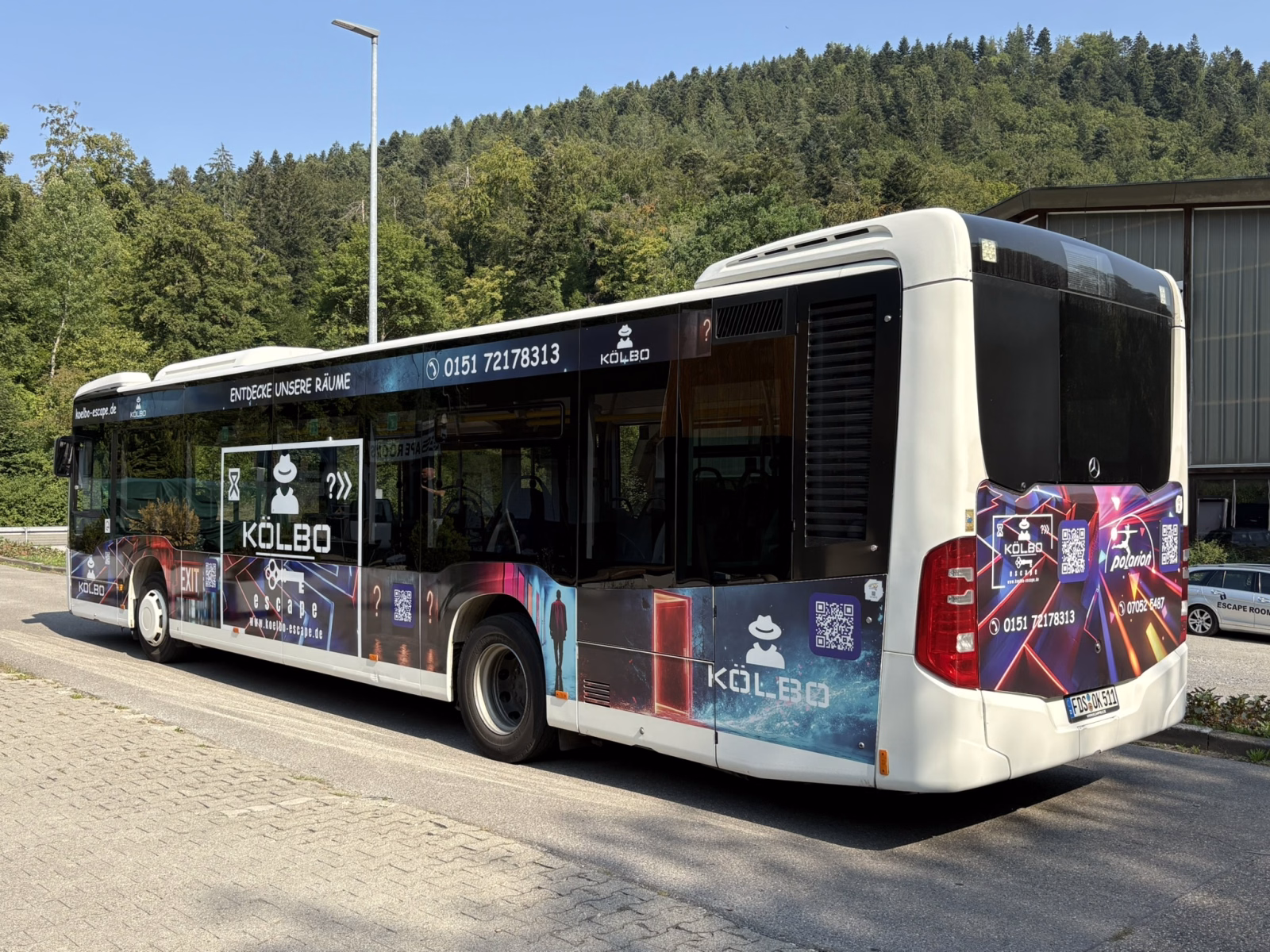 Heck- und Seitenansicht eines blauen Busses mit Werbung von Kölbo Escape