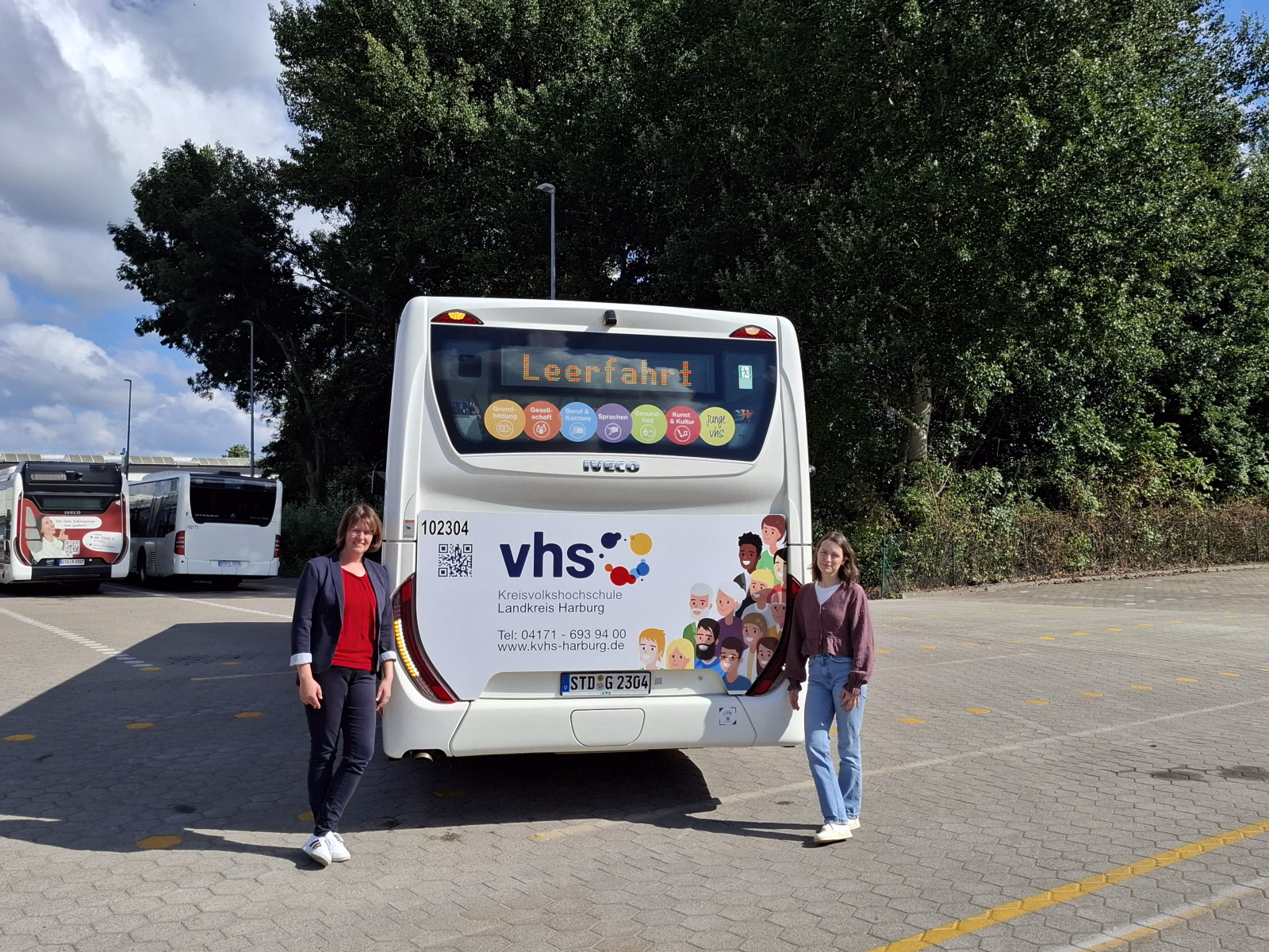 Zwei Frauen stehen vor dem Heck eines weißen Stadtbusses mit Werbung der Kreisvolkshochschule Harburg