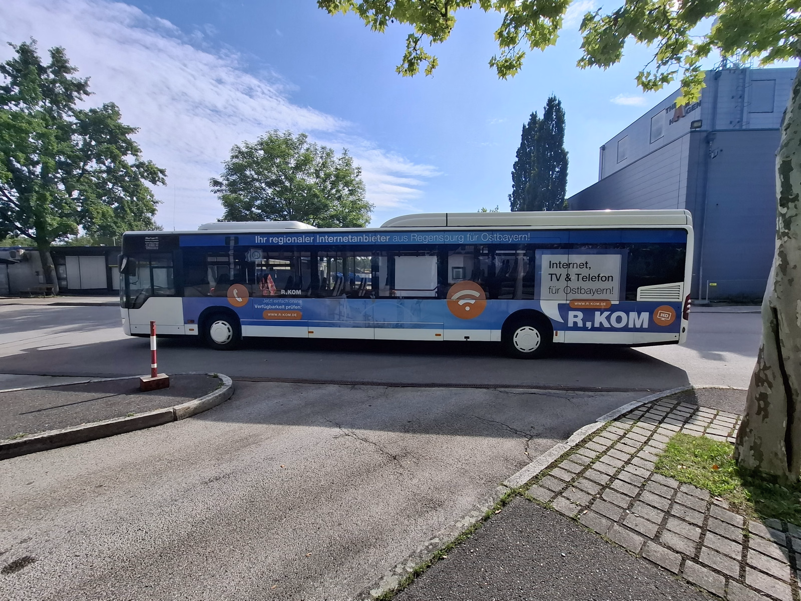Außenseite eines weißen Werbebusses mit blauer Werbung der R-Kom