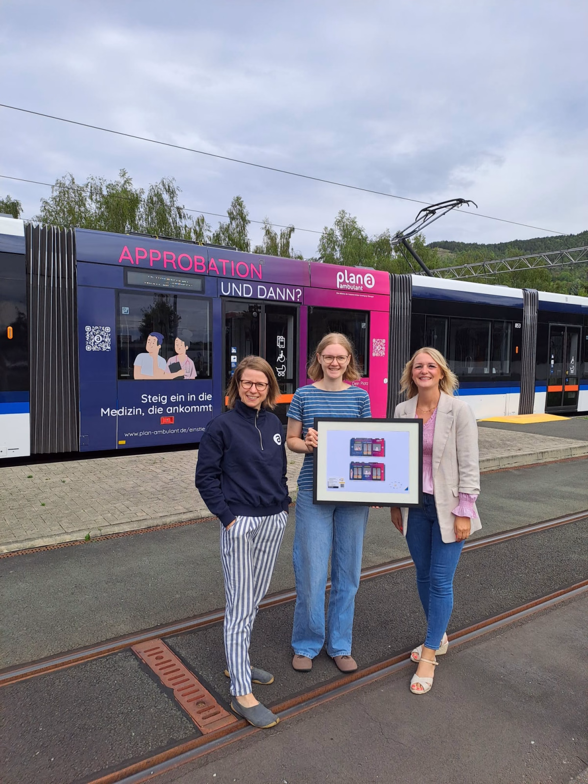 Drei Frauen stehen vor einer pinken Straßenbahn mit Werbung der kassenärtzlichen Vereinigung Thüringen